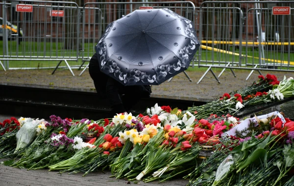 Цветы у мемориала и женщина под зонтом